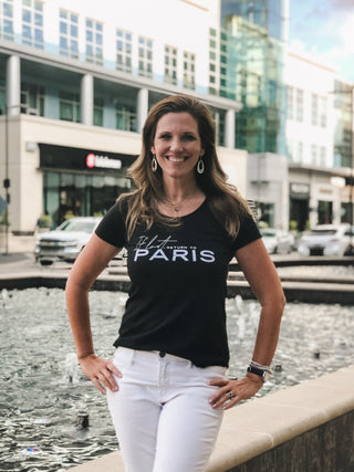 Woman wearing black scoop neck t-shirt with French saying If Lost Return to Paris