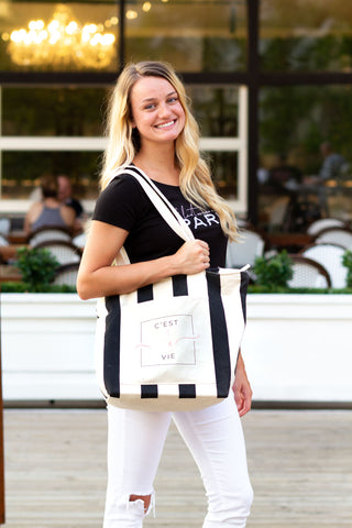Woman wearing black scoop neck t-shirt with French saying If Lost Return to Paris and striped C'est La Vie Bag